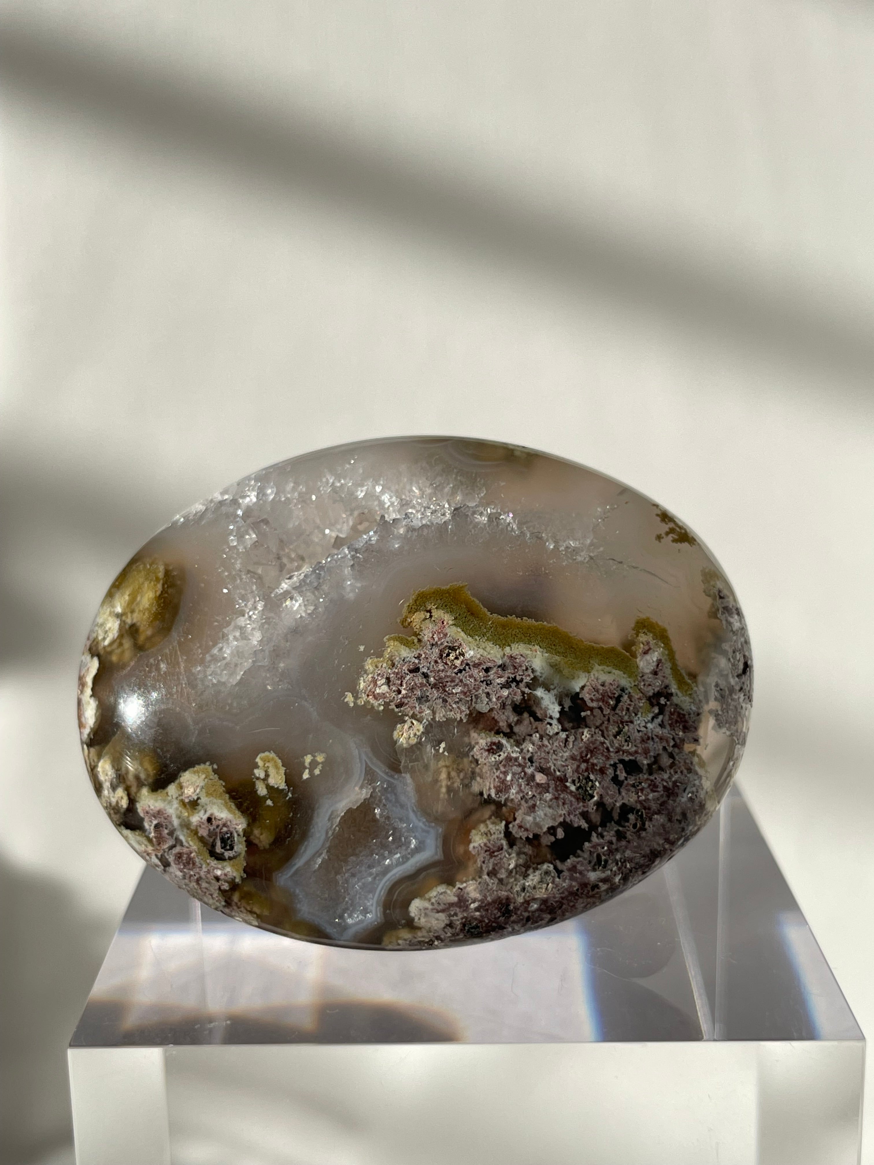 Scenic moss agate palm stone with earthy tones and intricate patterns, displayed on a clear stand.