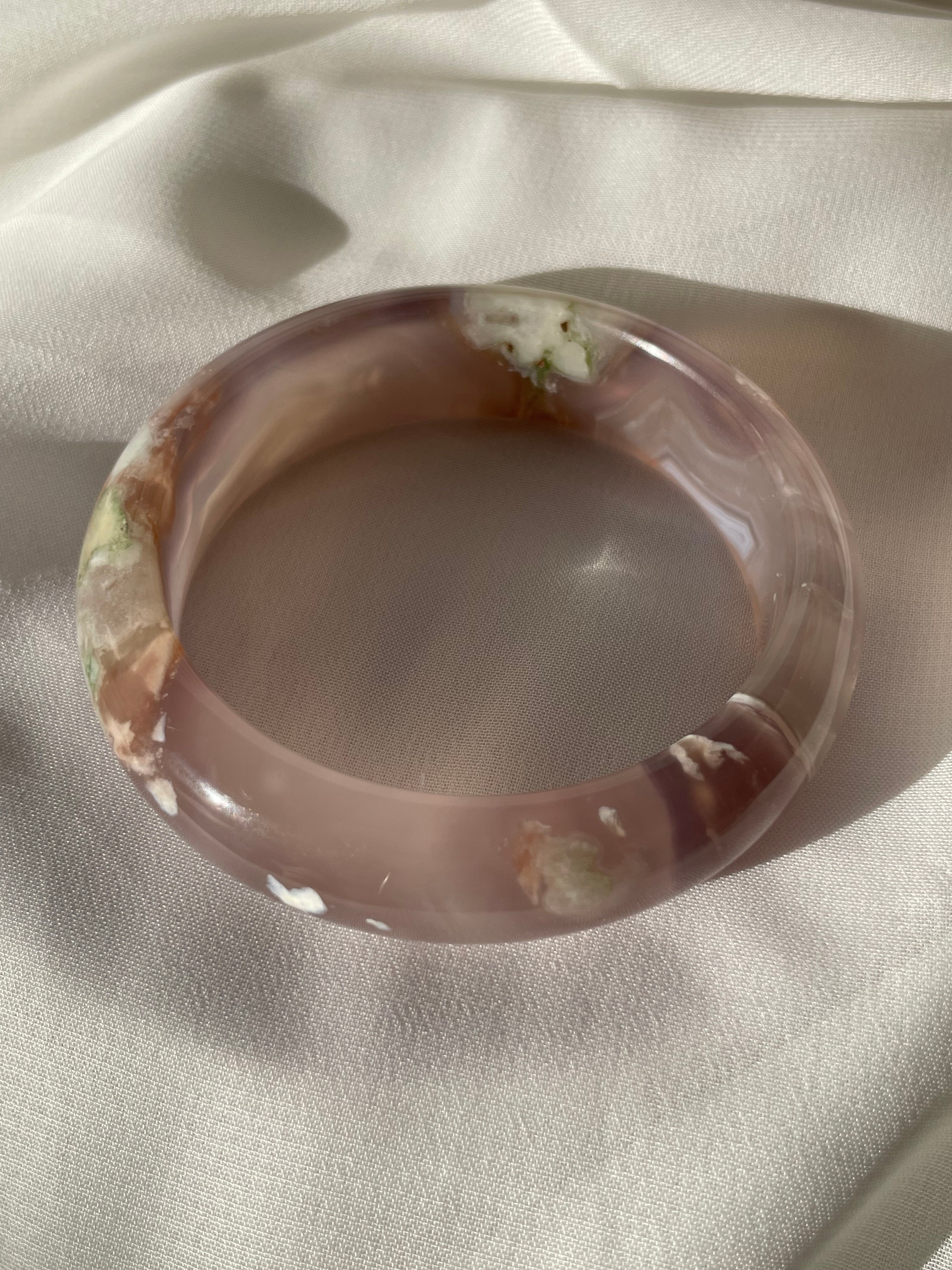 Beautiful flower agate bangle with soft pink and earthy tones, resting on a light fabric background.