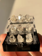 Nine mini Herkimer diamond crystal specimens displayed in a clear box, showcasing their natural beauty and clarity.
