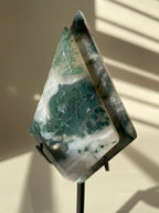 Scenic moss agate crystal specimen displayed on a stand, showcasing rich green patterns and natural beauty.