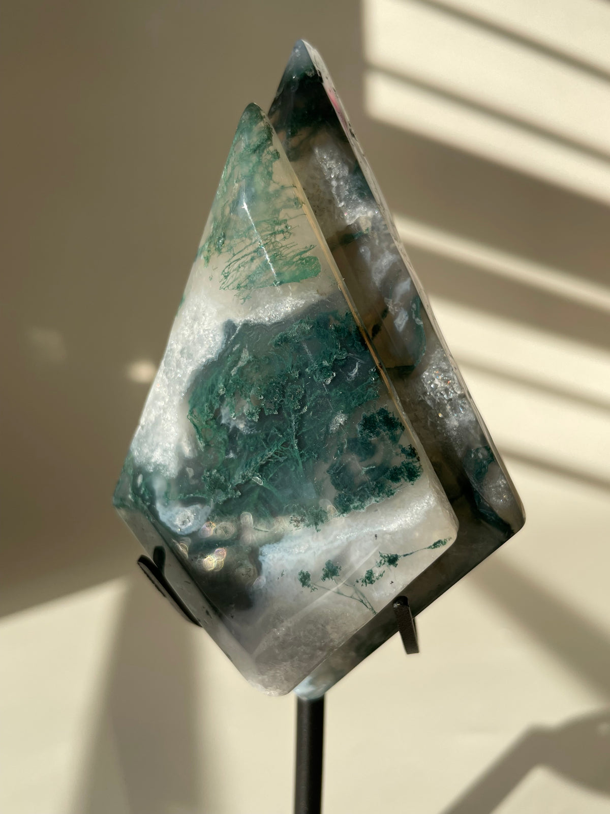 Scenic moss agate crystal specimen displayed on a stand, showcasing rich green patterns and natural beauty.