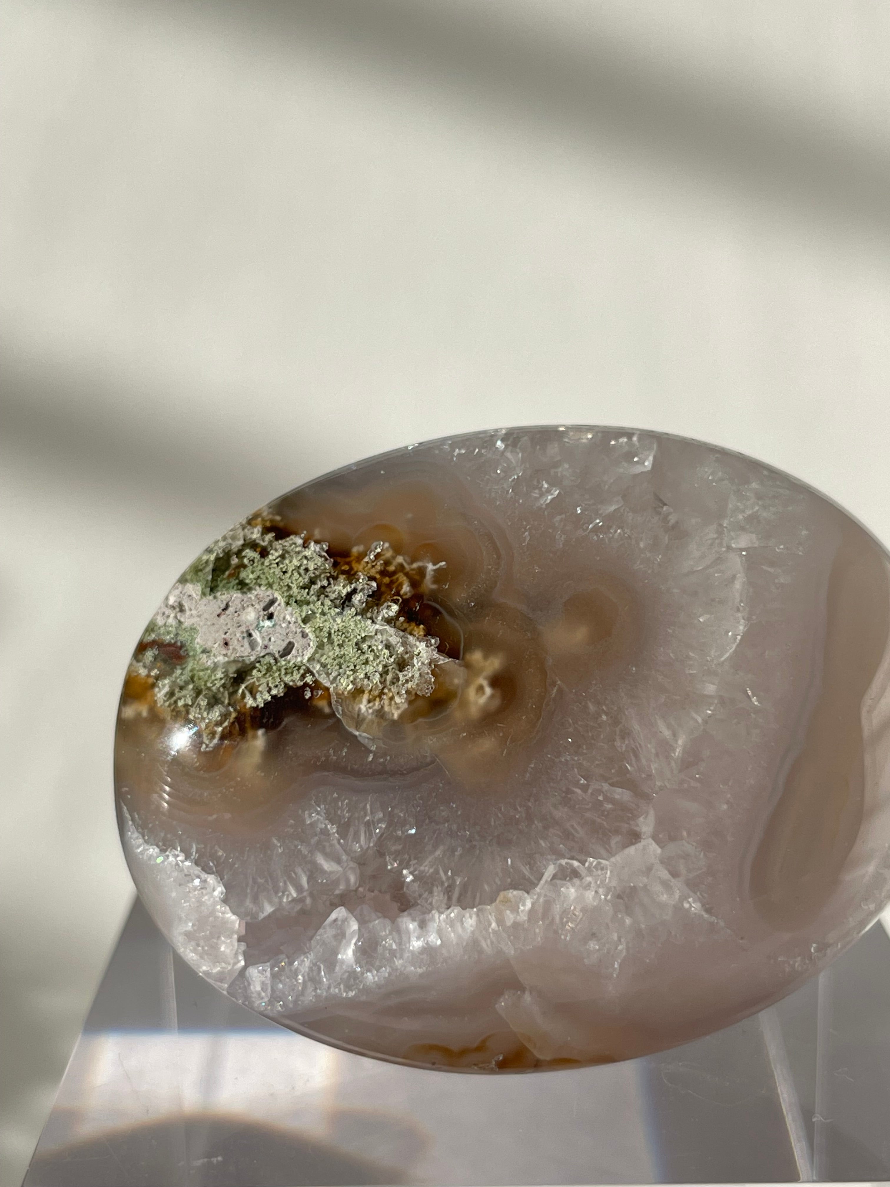 Scenic moss agate palm stone featuring earthy tones and unique patterns, displayed elegantly on a clear stand.
