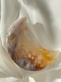 Beautiful flower agate moon with soft pink and orange hues resting on a silky white fabric.