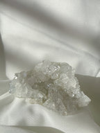 A sparkling apophyllite cluster with clear, crystalline formations resting on a soft, white fabric background.