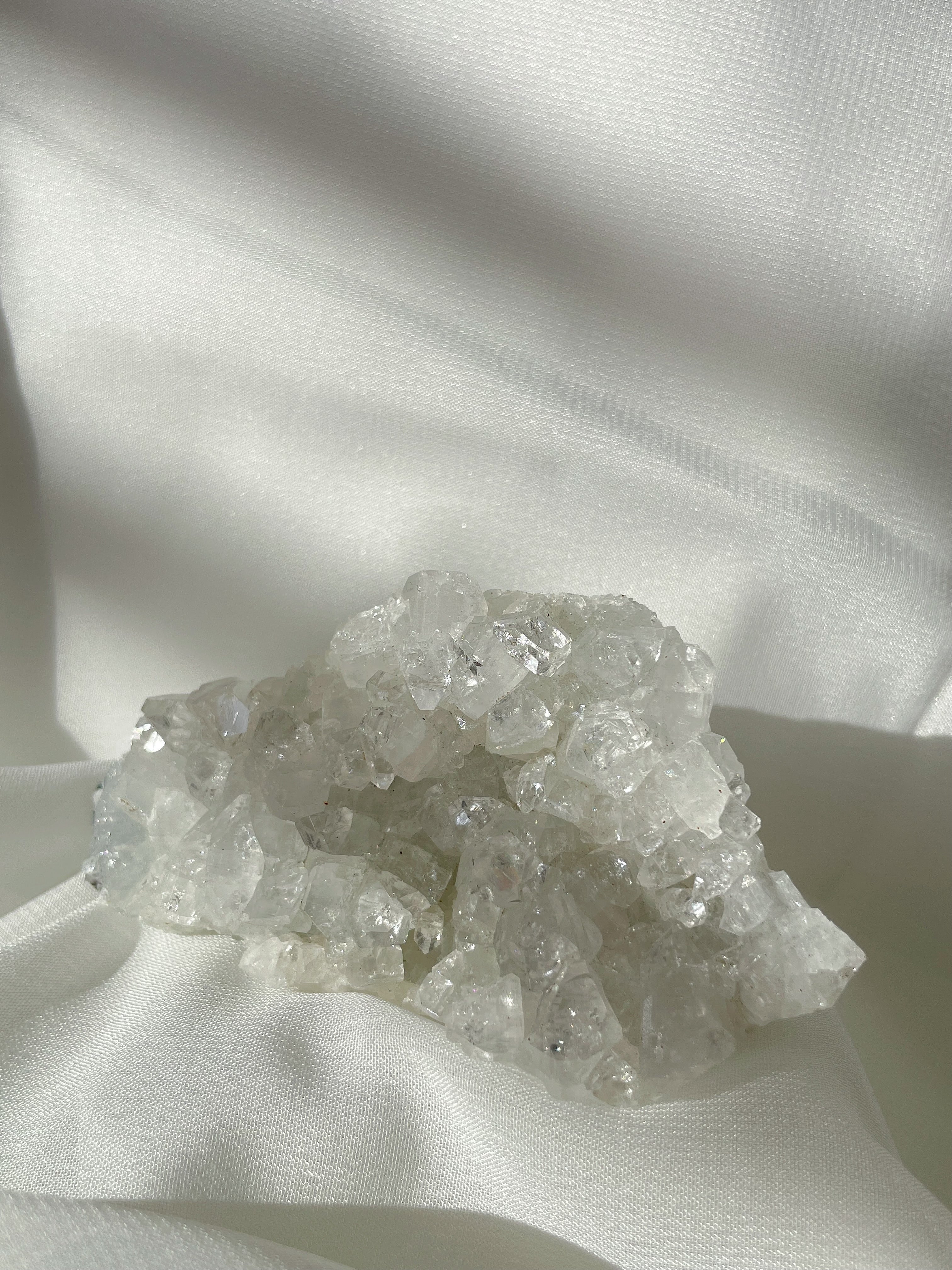 A sparkling apophyllite cluster with clear, crystalline formations resting on a soft, white fabric background.