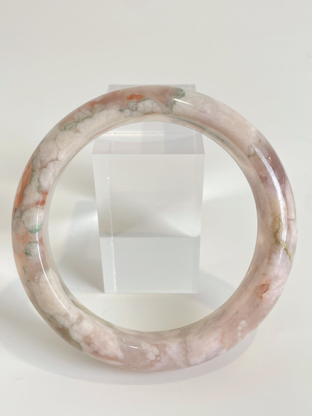 Beautiful flower agate bangle featuring soft pink and green hues, displayed against a clear stand.