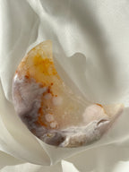 Beautiful flower agate moon with warm hues of orange and cream, resting on soft white fabric.