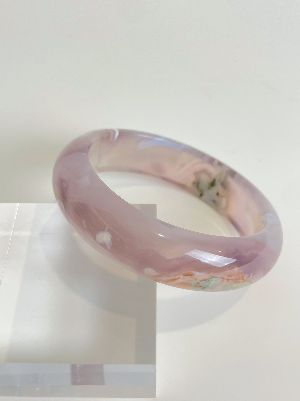 Beautiful flower agate bangle showcasing soft pink hues and natural patterns, resting on a clear display stand.