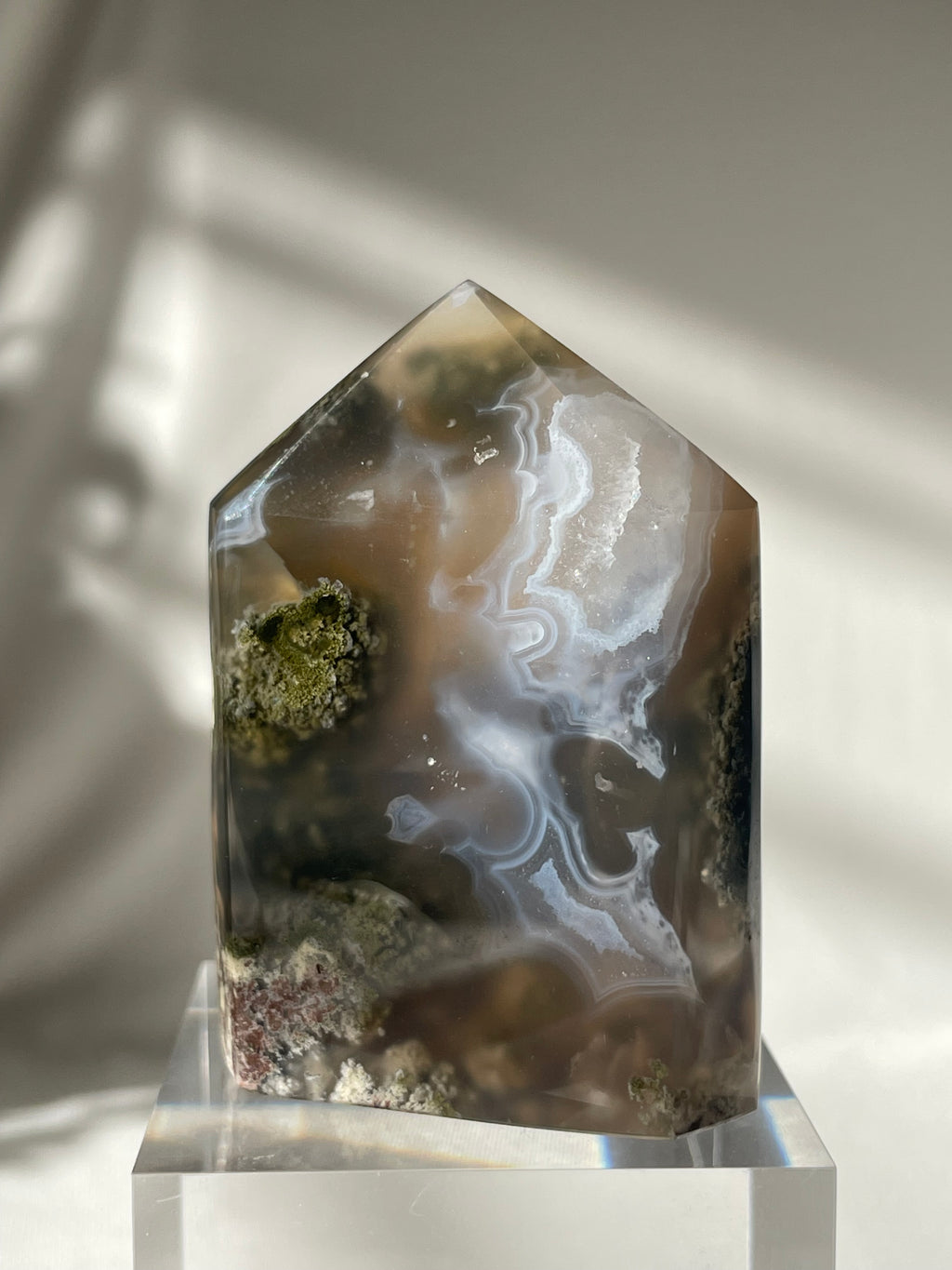 Scenic moss agate crystal tower with earthy tones and natural patterns, displayed on a clear base.