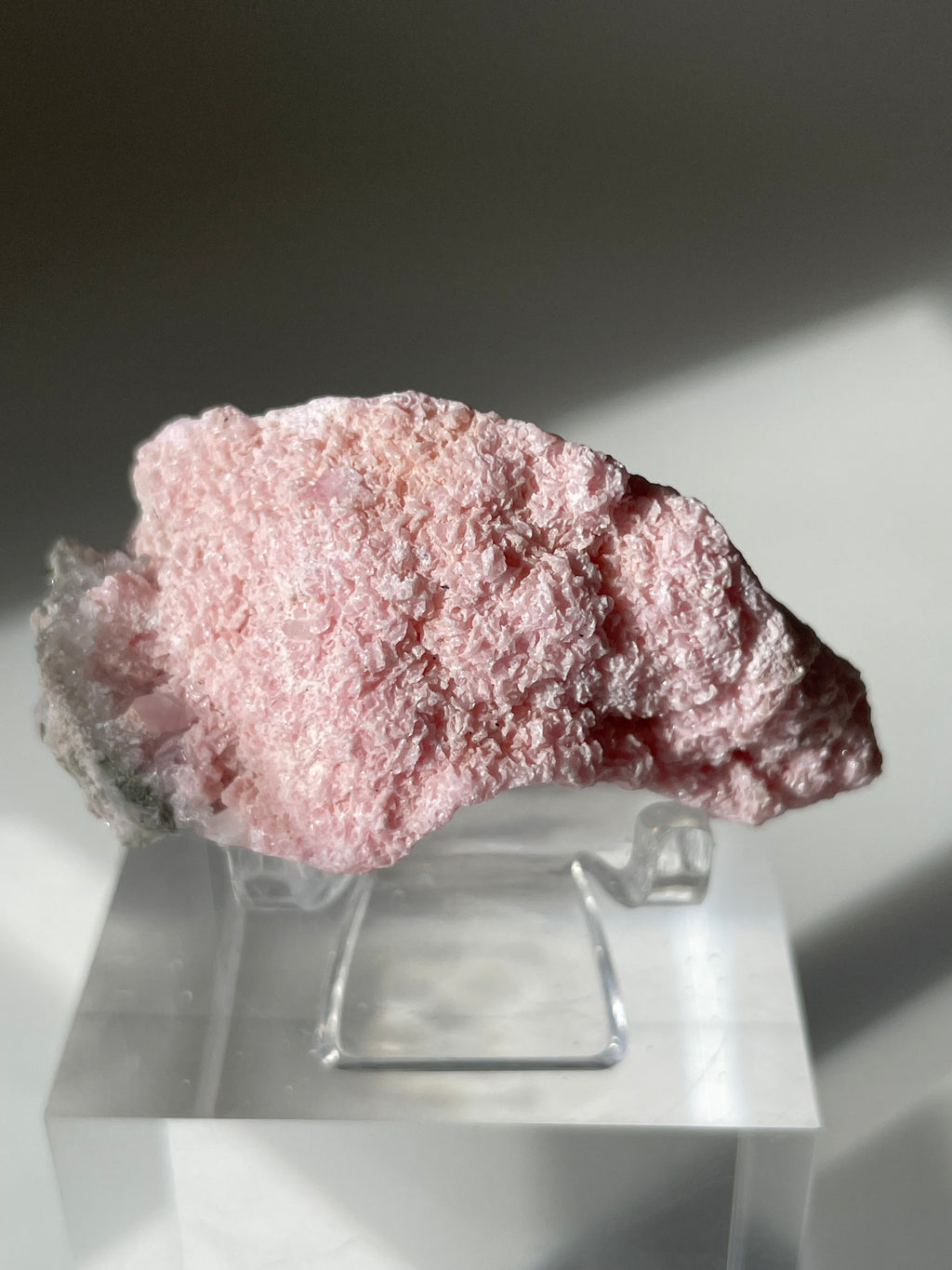 Beautiful rhodochrosite cluster with a soft pink hue, displayed on a clear stand, showcasing its natural texture.