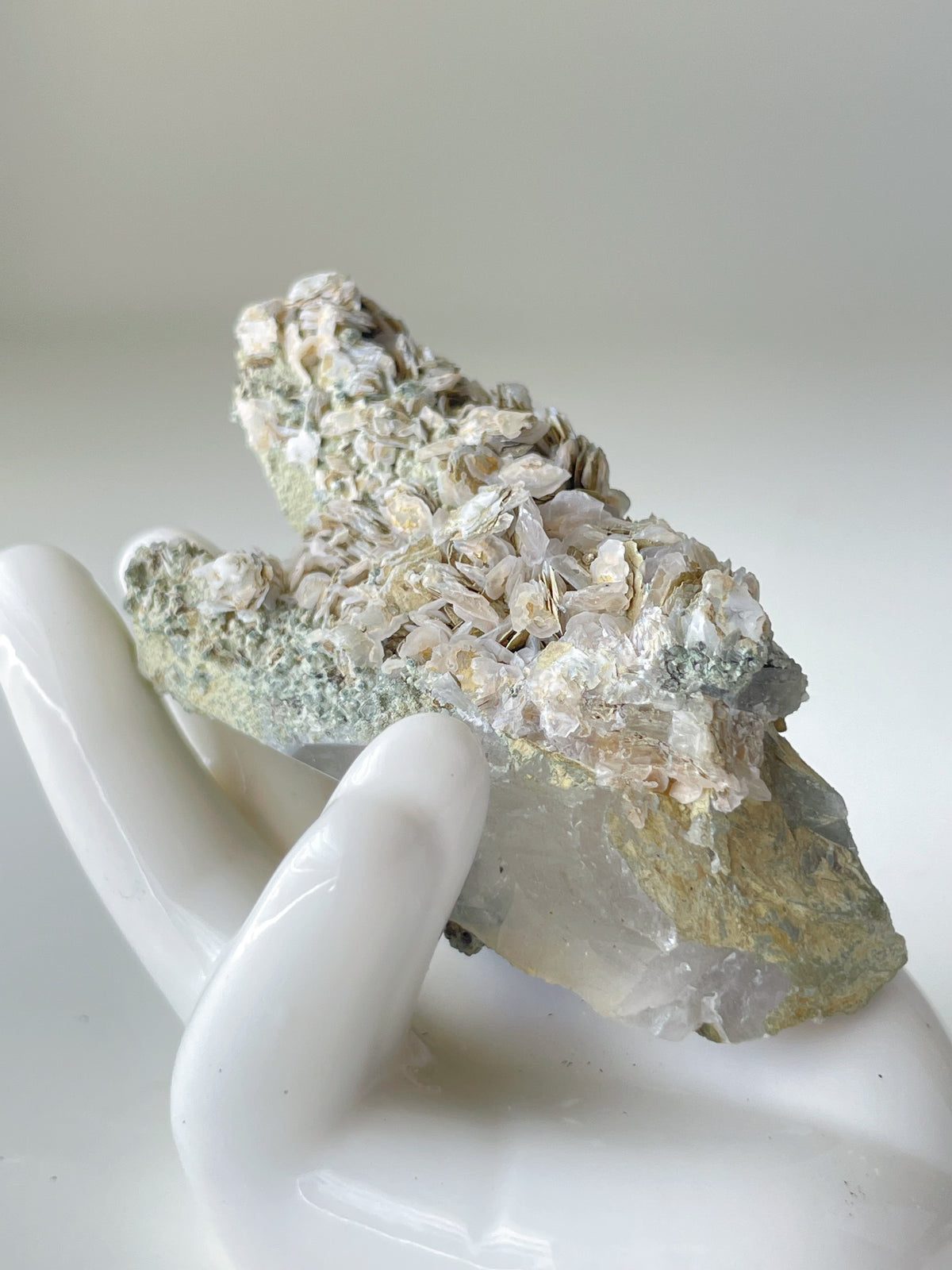 Rosette petal calcite specimen on quartz, showcasing delicate textures and natural colors, held in a white hand sculpture.