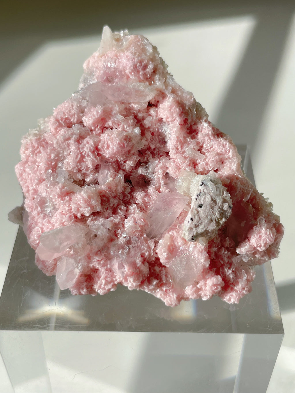 Rhodochrosite cluster with pink hues and crystal formations, displayed on a clear stand, showcasing its natural beauty.