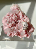 Rhodochrosite cluster with pink hues and crystal formations, displayed on a clear stand, showcasing its natural beauty.