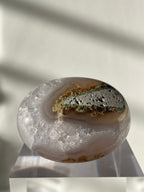 Scenic moss agate palm stone with earthy tones and natural patterns, displayed on a clear pedestal.