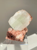 Beautiful pink Heulandite and Apophyllite crystal specimen displayed on a clear pedestal, showcasing its unique formations.