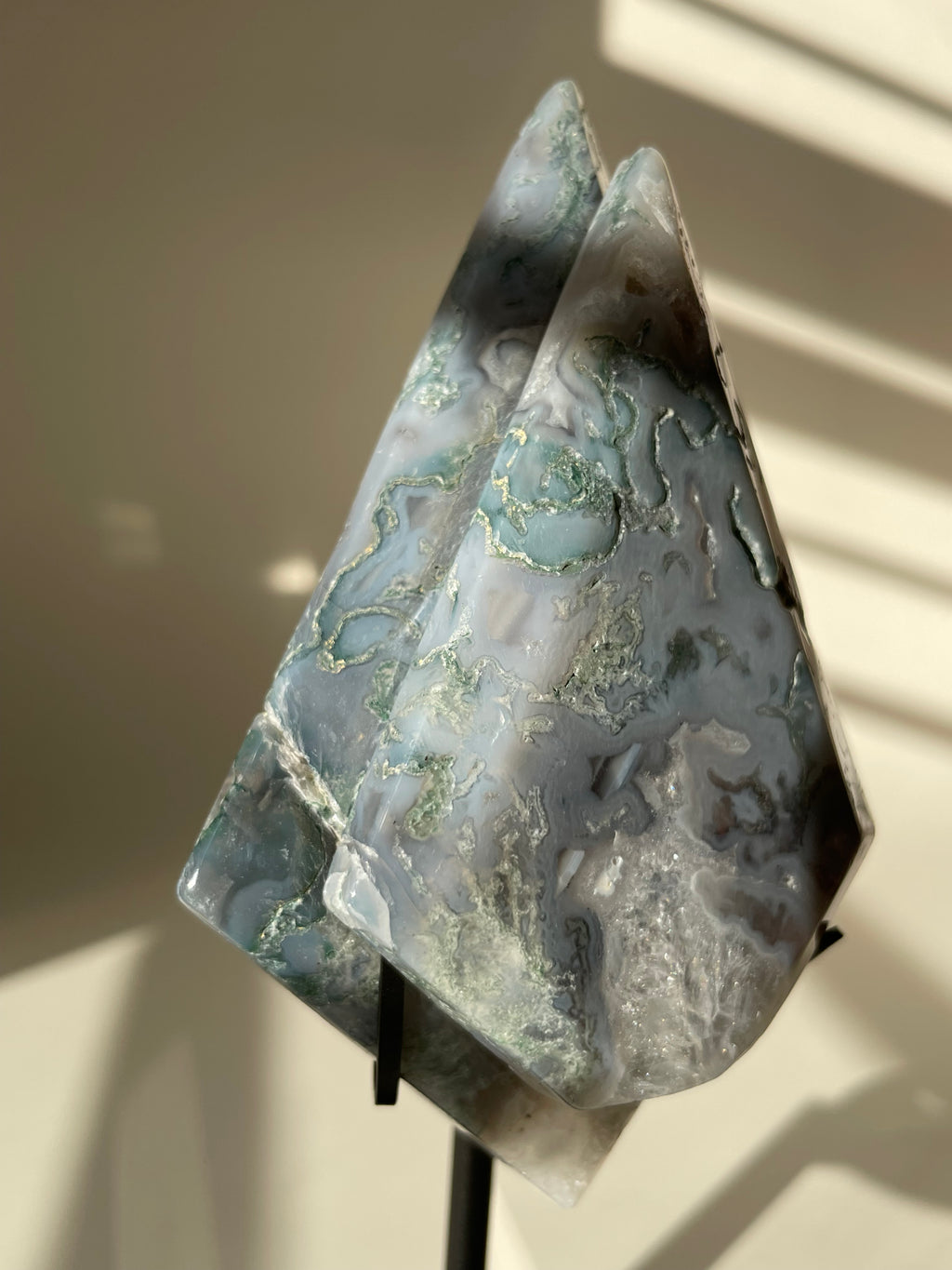Scenic moss agate crystal specimen displayed on a stand, showcasing its unique patterns and colors.