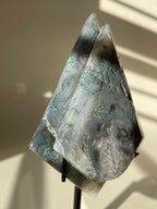 Scenic moss agate crystal specimen displayed on a stand, showcasing its unique patterns and colors.