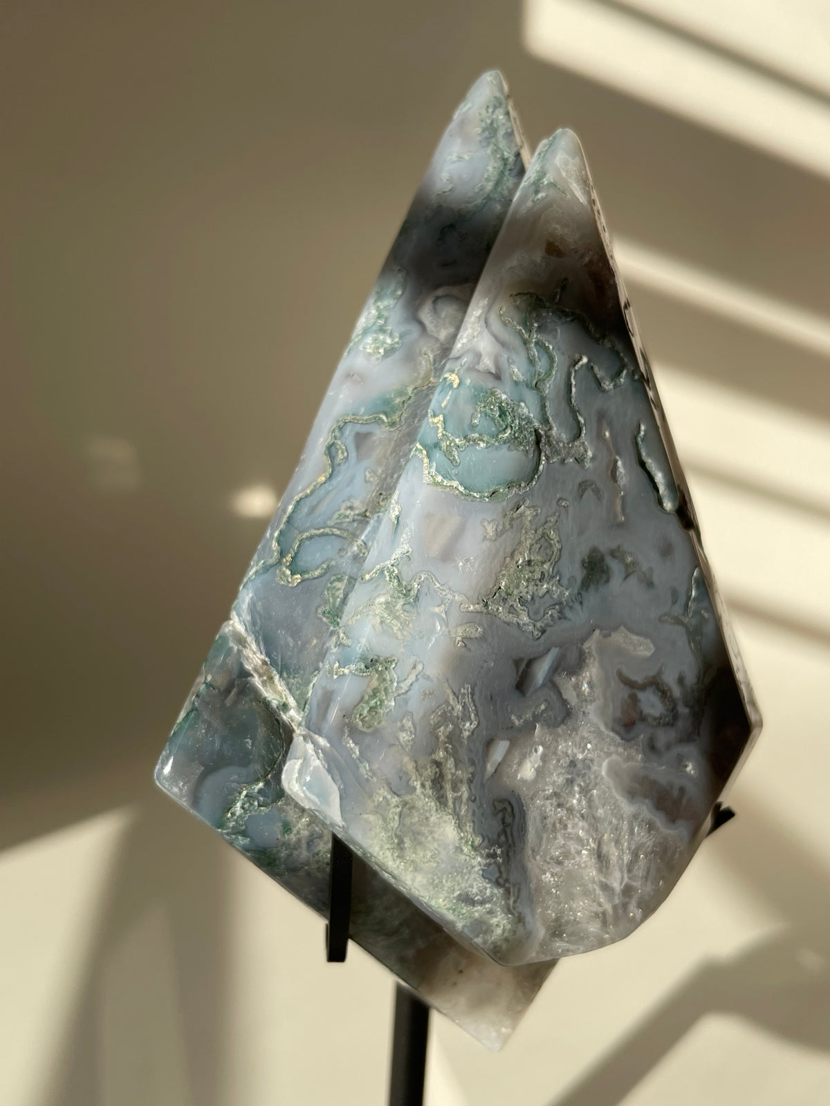 Scenic moss agate crystal specimen displayed on a stand, showcasing its unique patterns and colors.