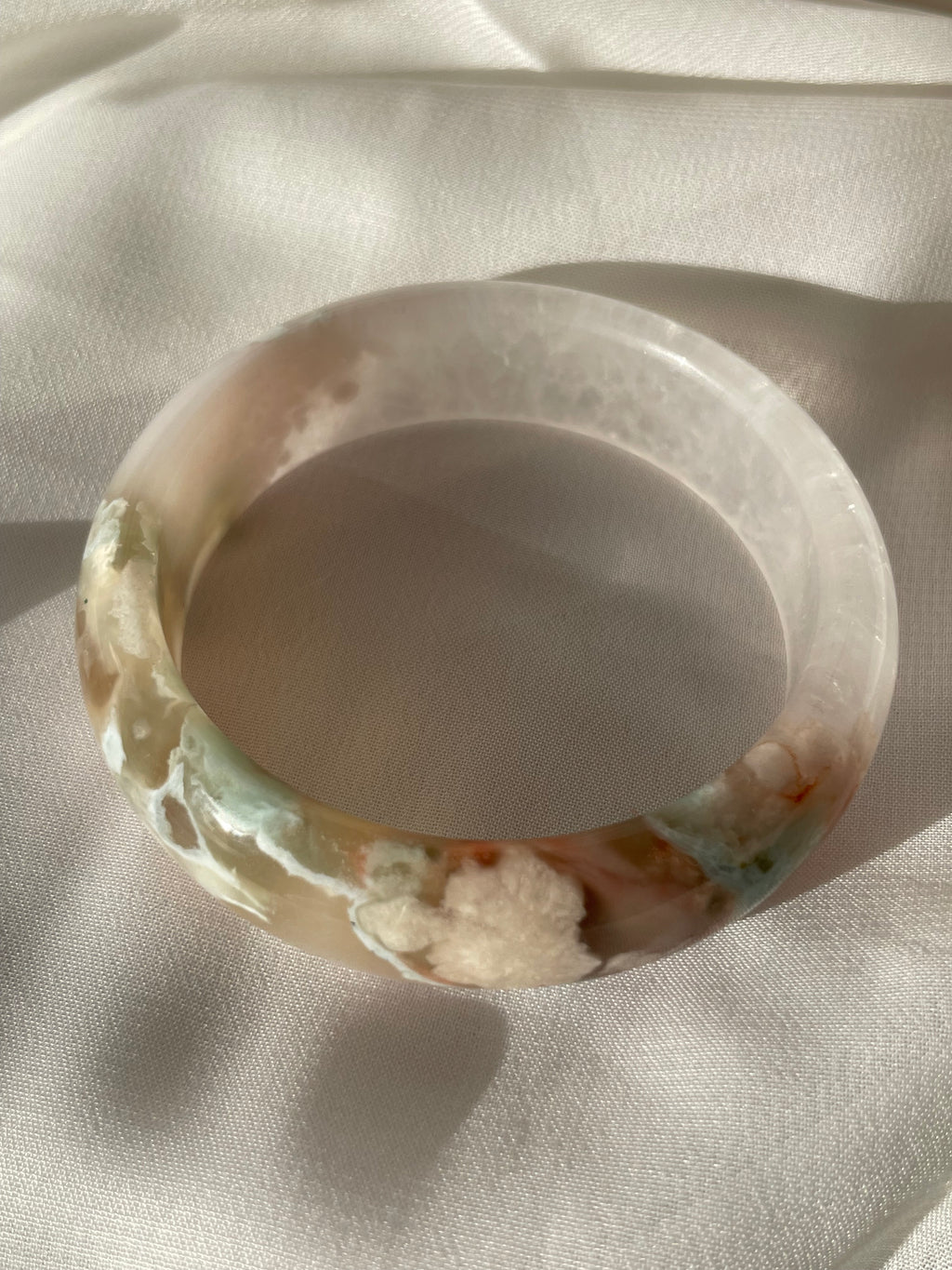 Beautiful flower agate bangle showcasing soft pink and earthy tones, resting on a light fabric background.