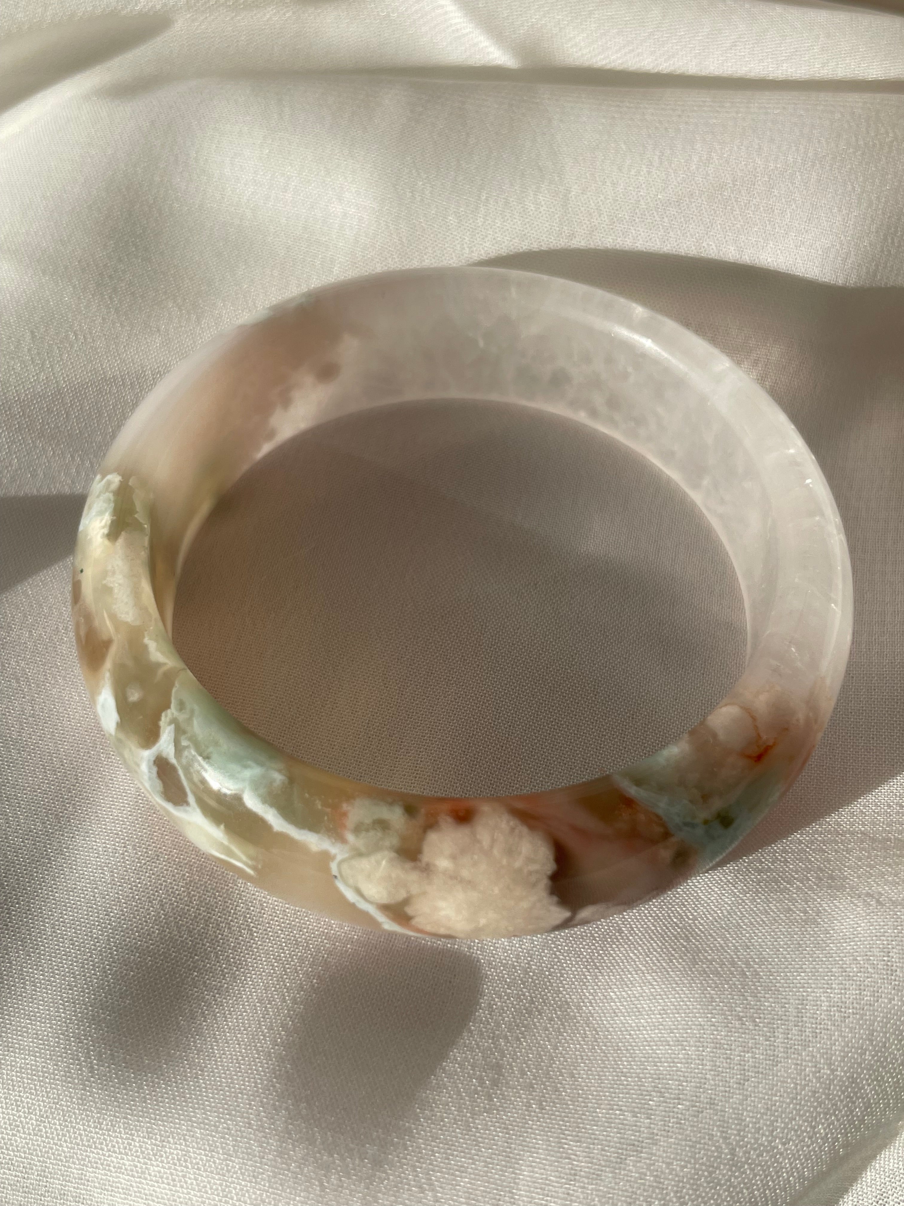 Beautiful flower agate bangle showcasing soft pink and earthy tones, resting on a light fabric background.