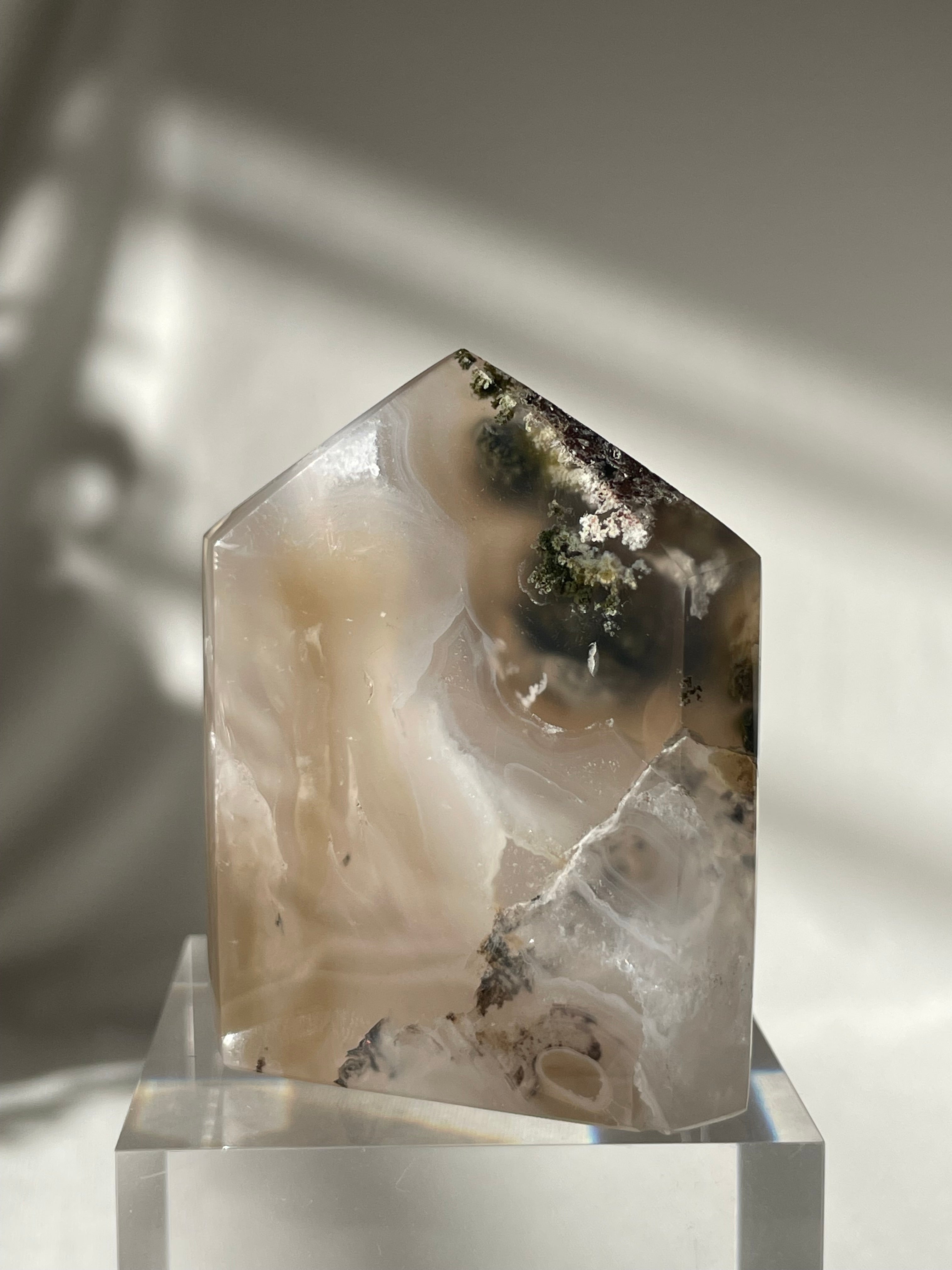 Scenic moss agate tower with earthy tones and natural patterns, displayed on a clear pedestal.