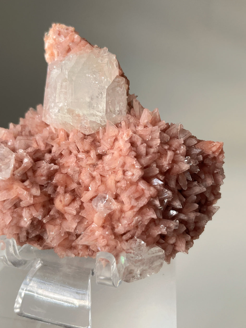 Beautiful pink Heulandite and Apophyllite crystal specimen with a textured surface, displayed on a clear stand.