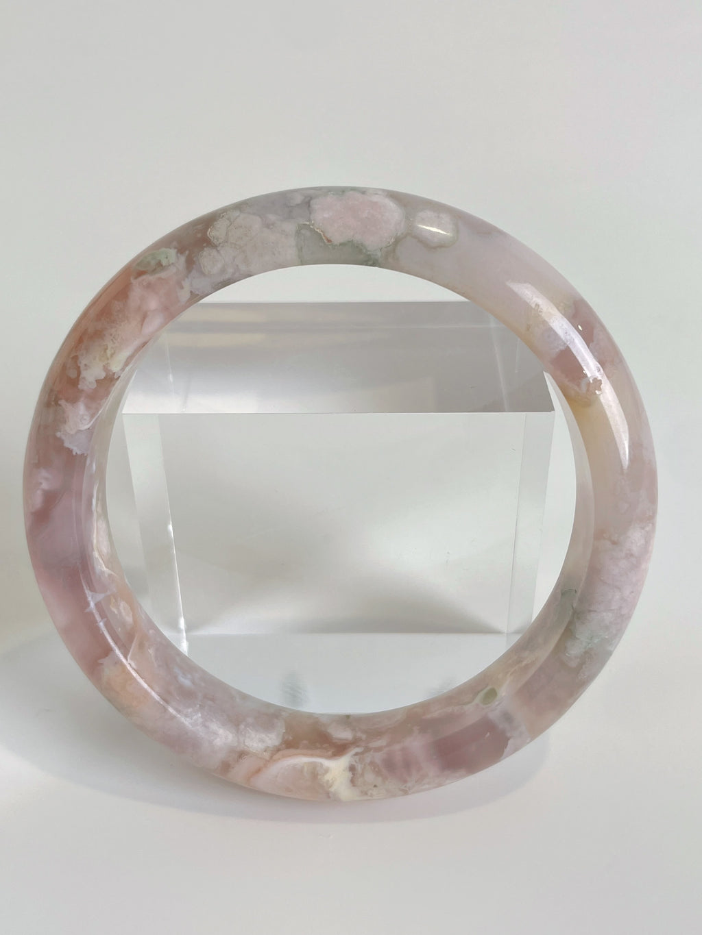 Beautiful flower agate bangle showcasing soft pink and green hues, displayed on a clear stand.