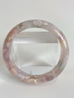 Beautiful flower agate bangle showcasing soft pink and green hues, displayed on a clear stand.