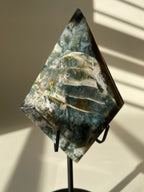 Scenic moss agate crystal specimen displayed on a stand, showcasing unique green and white patterns.