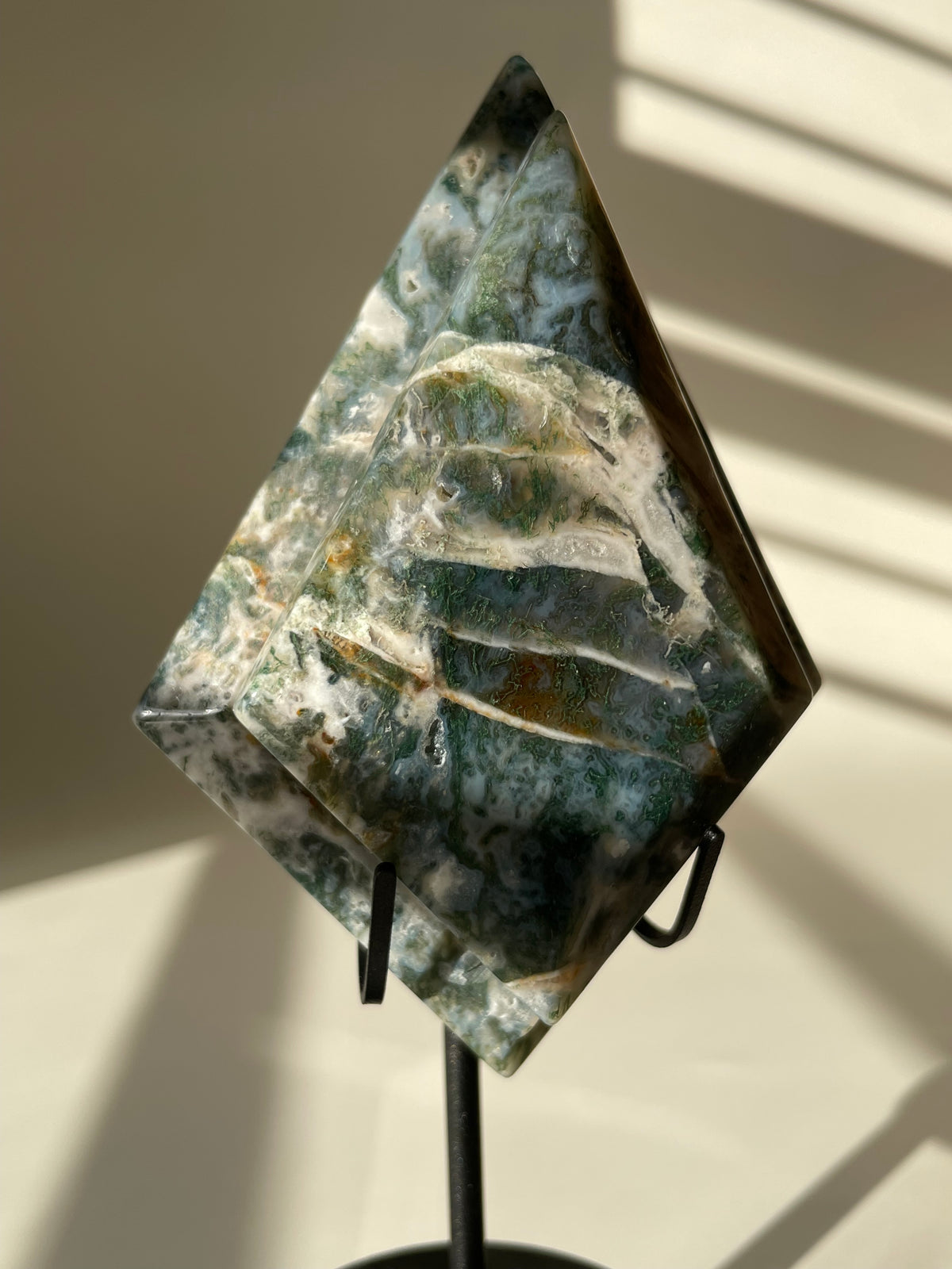 Scenic moss agate crystal specimen displayed on a stand, showcasing unique green and white patterns.