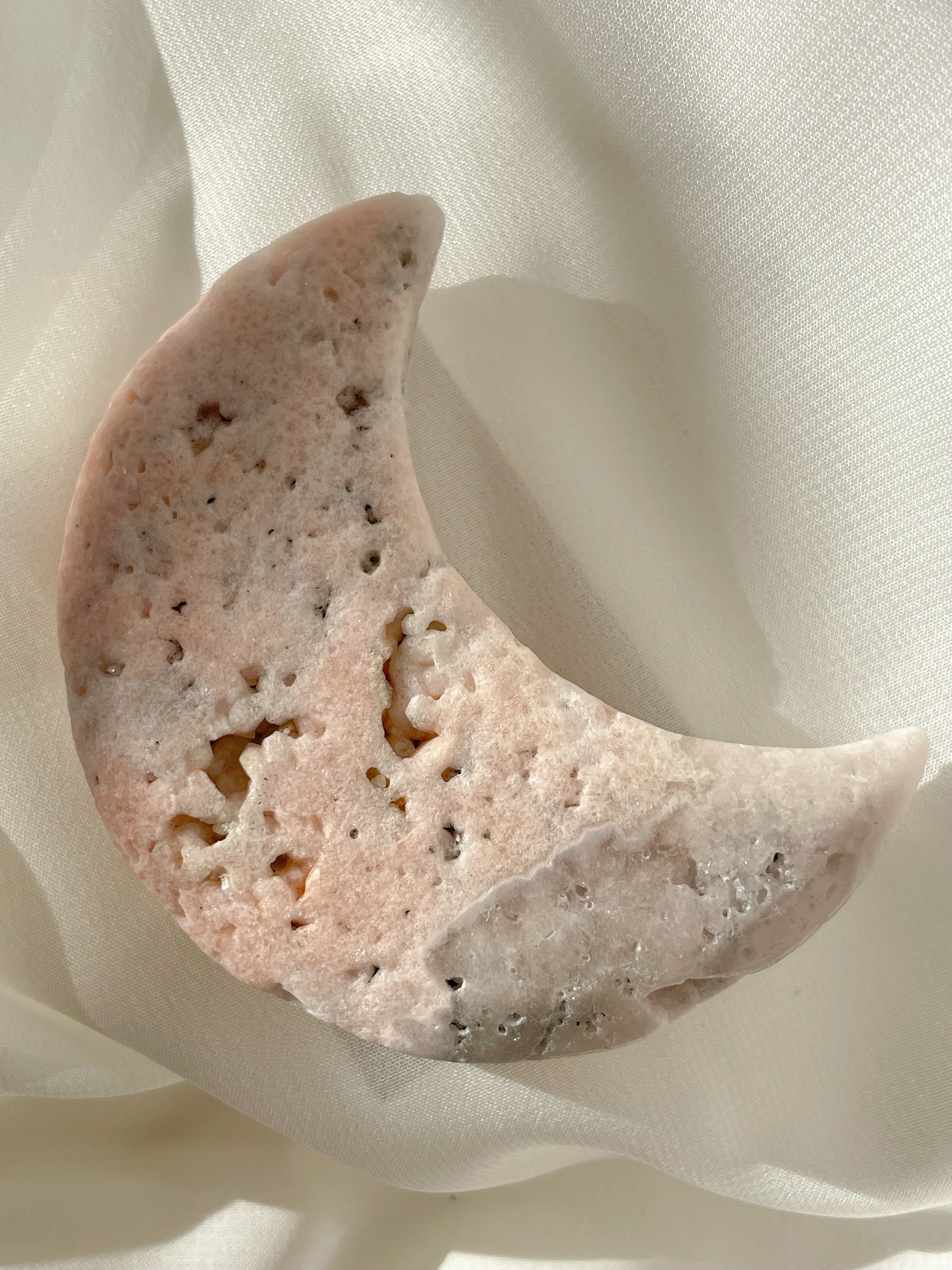 Beautiful flower agate moon with soft pink hues resting on a delicate white fabric.