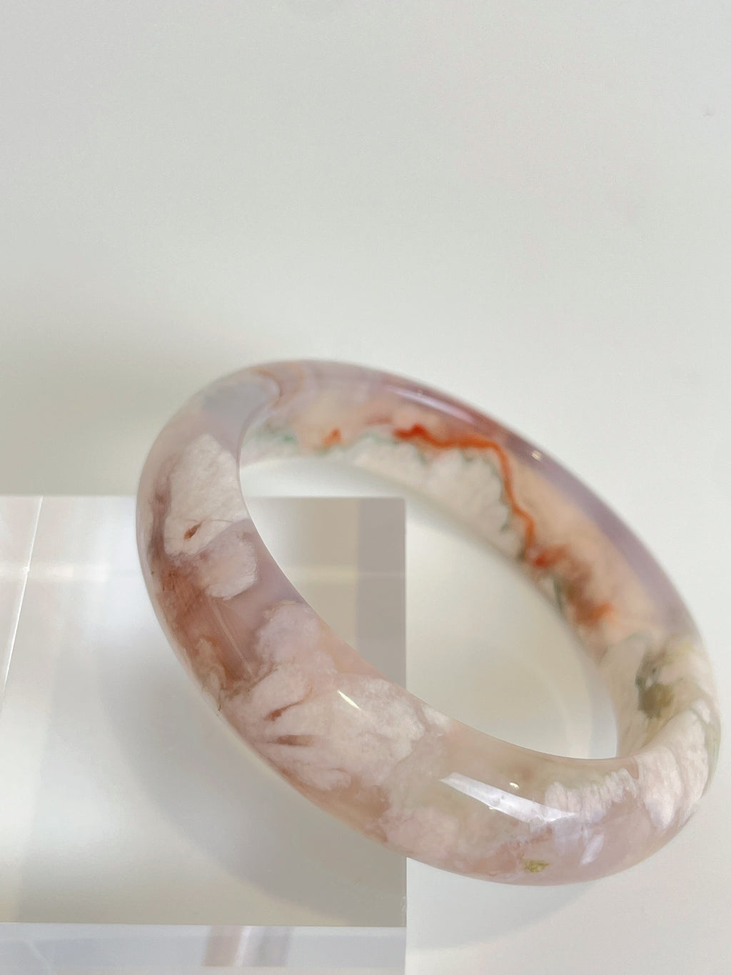 Beautiful flower agate bangle showcasing soft pink and white patterns, displayed on a clear stand.
