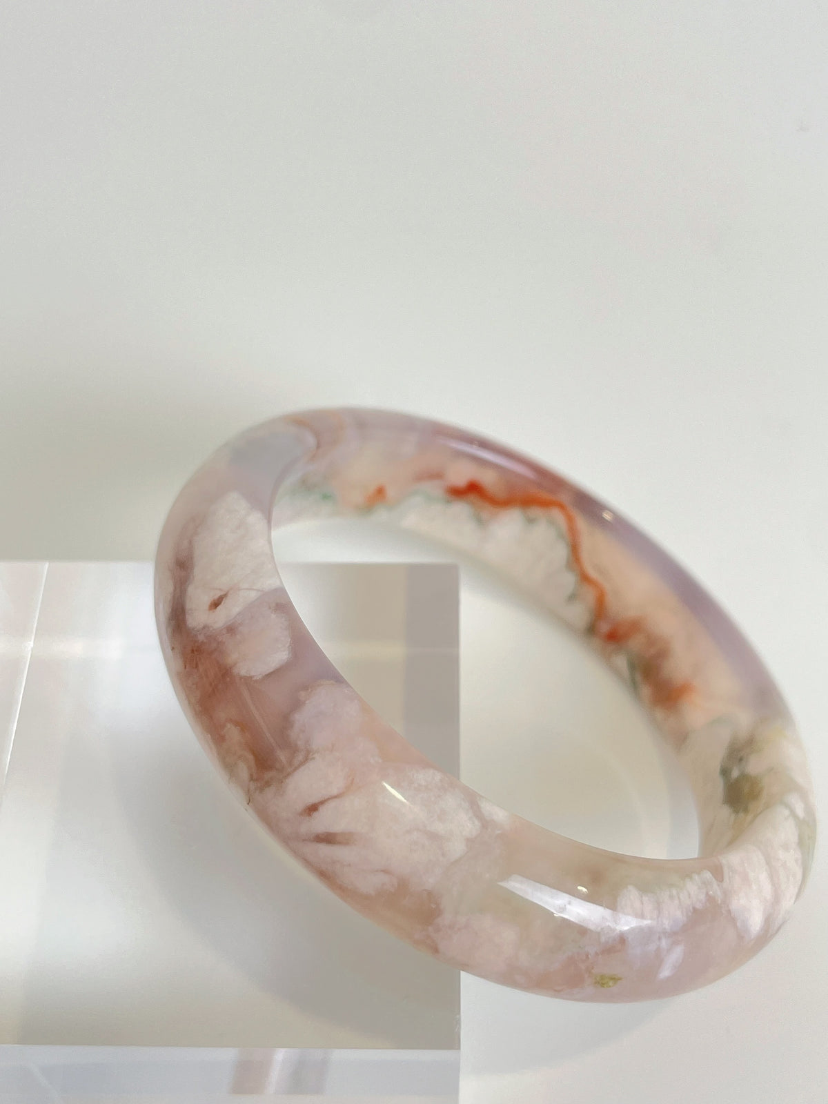 Beautiful flower agate bangle showcasing soft pink and white patterns, displayed on a clear stand.