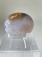 Scenic moss agate palm stone displayed on a clear stand, showcasing its unique patterns and colors.