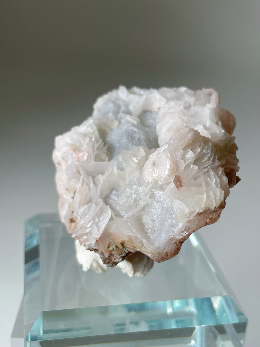 Beautiful pink petal calcite specimen on quartz, displayed on a clear pedestal, showcasing its unique texture and colors.