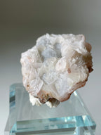 Beautiful pink petal calcite specimen on quartz, displayed on a clear pedestal, showcasing its unique texture and colors.