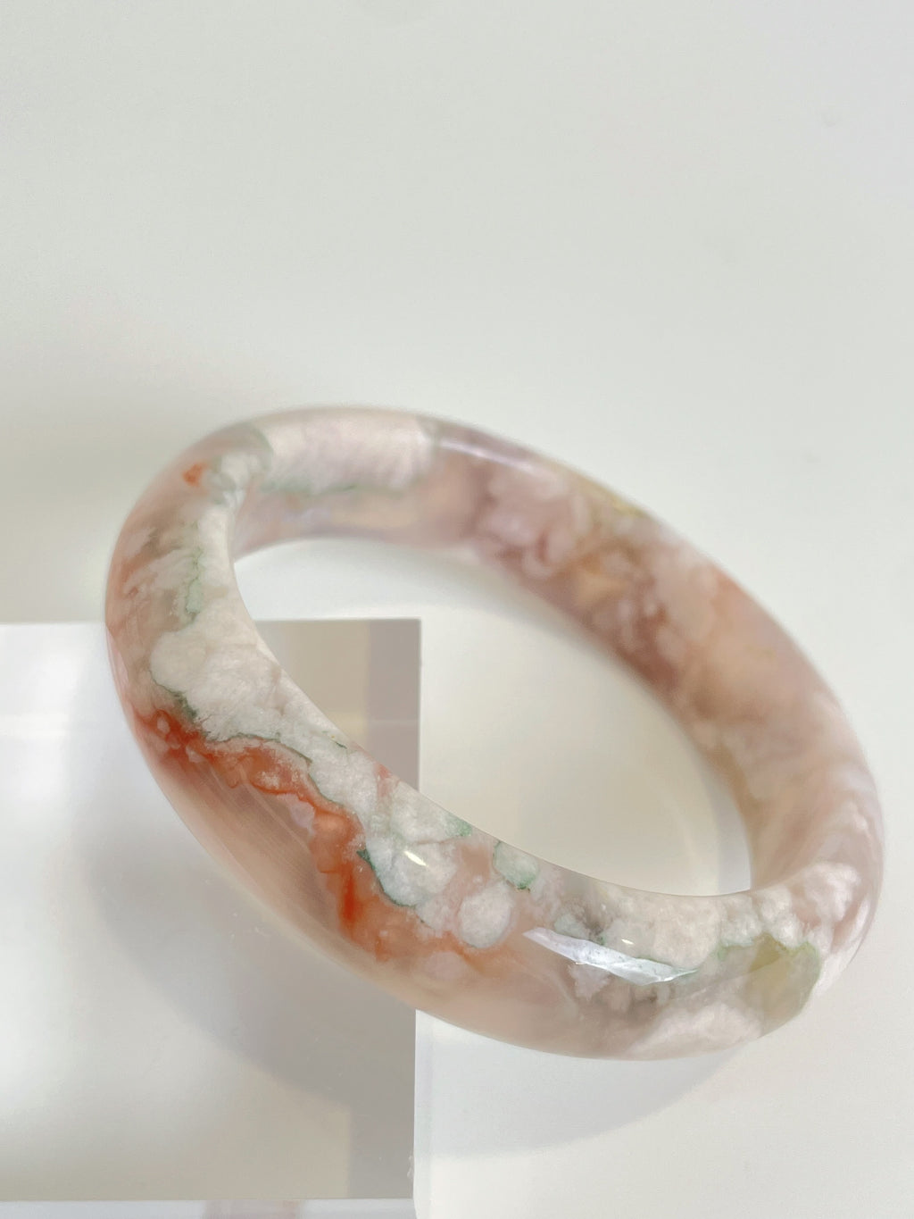 Beautiful flower agate bangle showcasing soft pink and earthy tones, elegantly displayed on a clear stand.