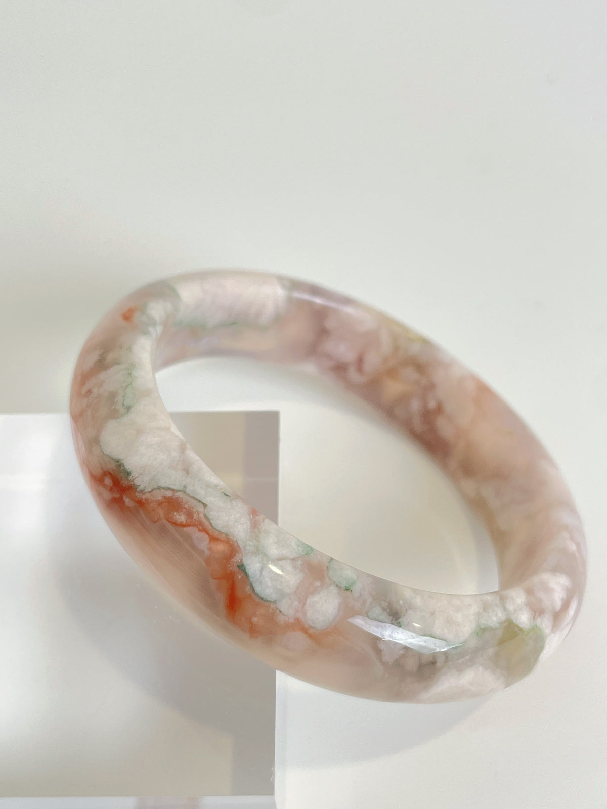Beautiful flower agate bangle showcasing soft pink and earthy tones, elegantly displayed on a clear stand.