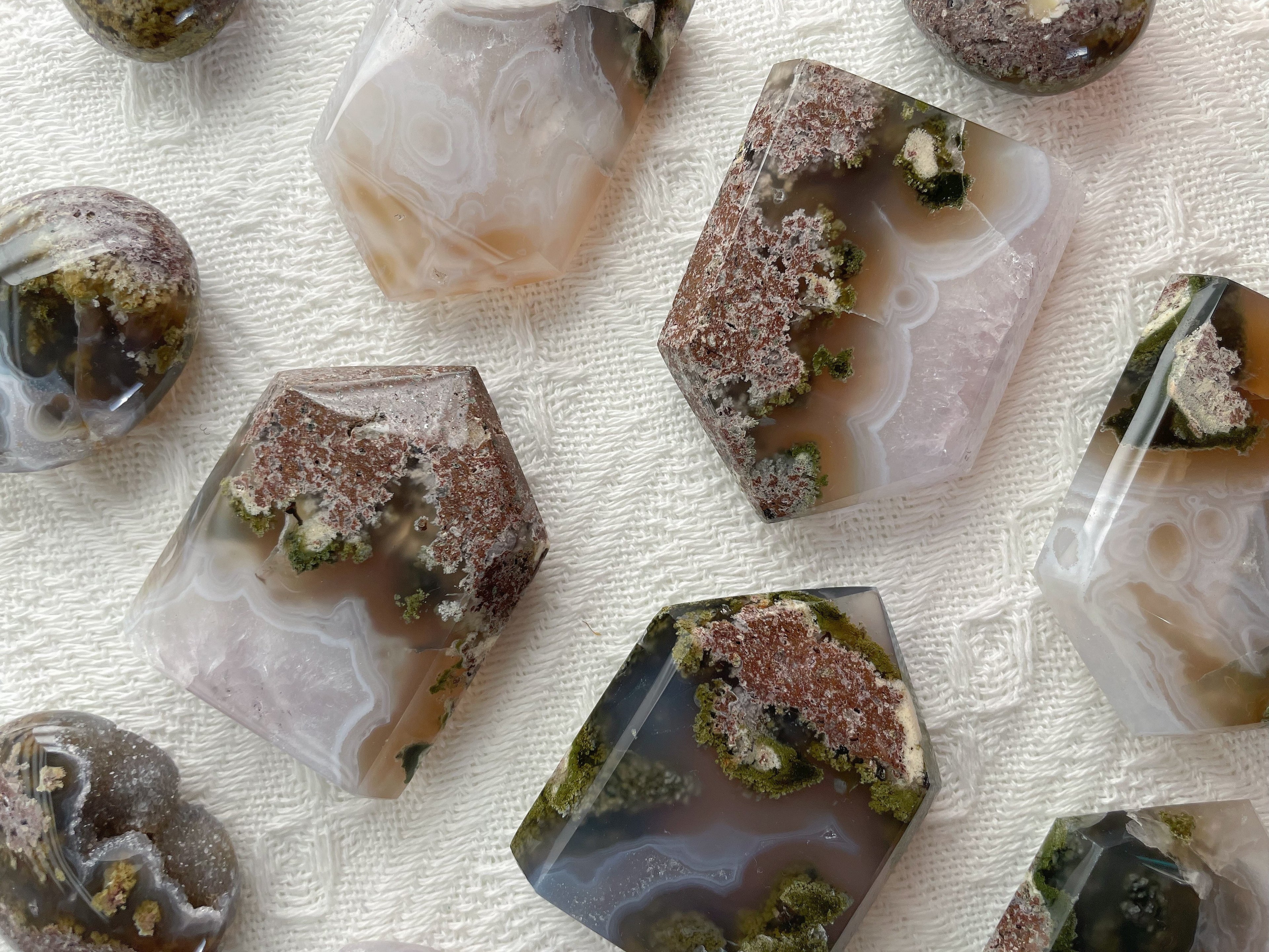 Several polished agate stone tiles with natural banding and crystalline formations, arranged on a textured off-white fabric background.